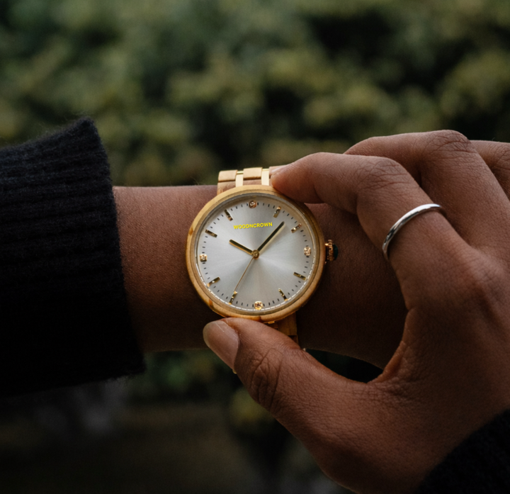 Gold wristwatch on a person's wrist with a blurred green background