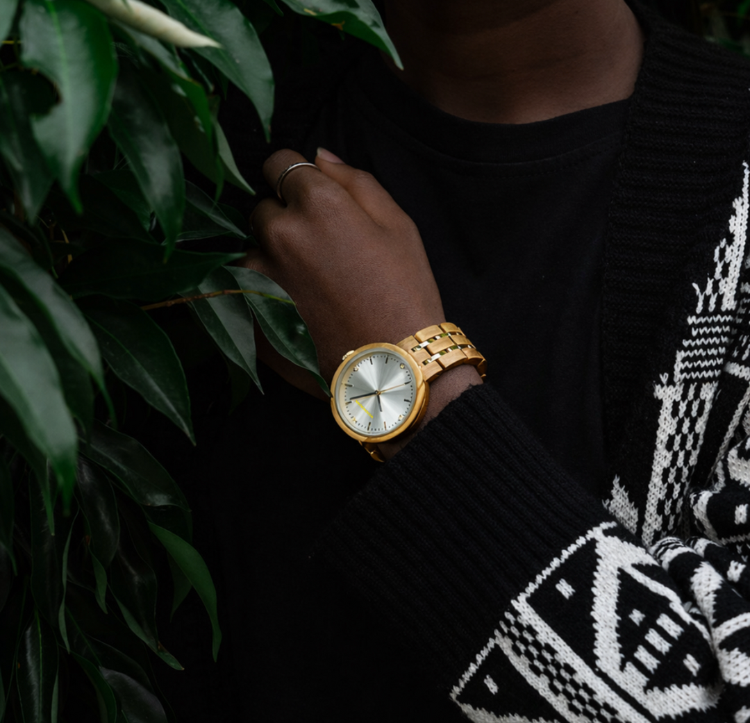 Person wearing a gold watch with a black and white patterned sleeve, holding green leaves.